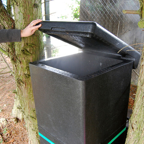 Person opening a black compost bin next to trees