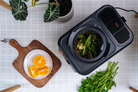 Electric composter on a white tiled surface with food and ingredients.
